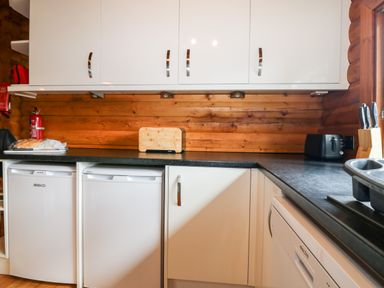 A kitchen with white cabinets black countertop a toaster bread a knife block and refrigerators at Rocksite in Kirkmichael Perth And Kinross