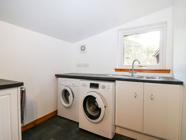 A utility room with a washing machine and dryer under a countertop with a sink below a window at Rocksite in Kirkmichael Perth And Kinross
