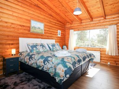 A bedroom with a large bed featuring animal print bedding a nightstand with a lamp wooden walls and a large window at Rocksite Kirkmichael Perth And Kinross