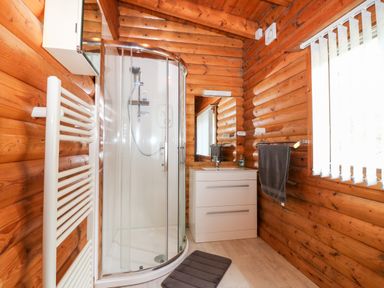 A bathroom with a curved glass shower enclosure a white sink cabinet a mirror and a window with vertical blinds at Rocksite in Kirkmichael Perth And Kinross