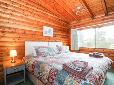 A bedroom with a double bed with patterned bedding beside a wooden nightstand with a lamp in a wooden cabin at Rocksite in Kirkmichael Perth And Kinross