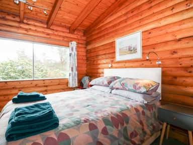 A bedroom with a double bed two teal towels on the bed a bedside table and a large window at Rocksite in Kirkmichael Perth And Kinross