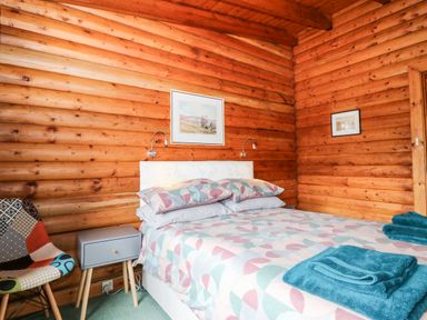 A bedroom with a double bed, a bedside table, a chair, and artwork on wooden log walls at Rocksite Kirkmichael Perth And Kinross