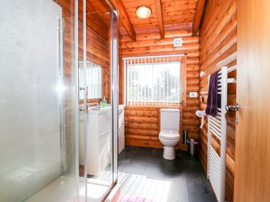 A bathroom with a shower, sink with cabinet, toilet, window with blinds, towel rail, and wooden walls at Rocksite Kirkmichael Perth And Kinross