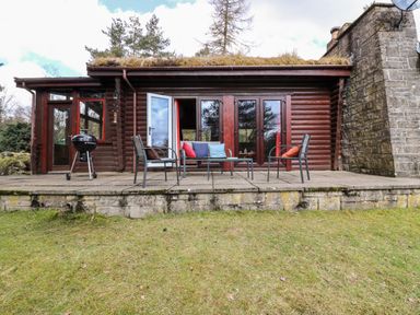 A patio area with chairs and a barbecue outside a wooden cabin at Rocksite in Kirkmichael Perth And Kinross
