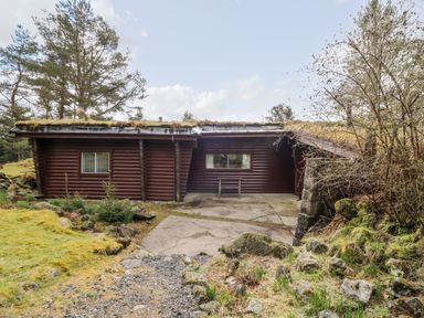 A wooden cabin surrounded by trees and rocks with a concrete area in front at Rocksite in Kirkmichael Perth And Kinross