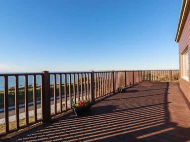 A wooden deck with railings and flower pots overlooking the sea at Sunset Sea View Chalet in Millbrook