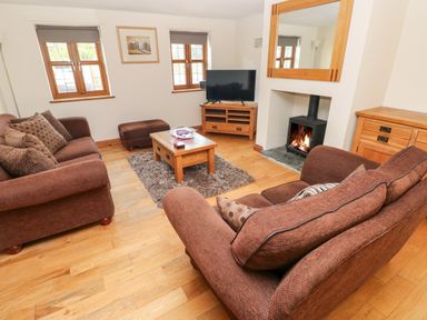 A living room with two brown sofas a wooden coffee table and a burning fireplace at Ty Melyn in Boncath