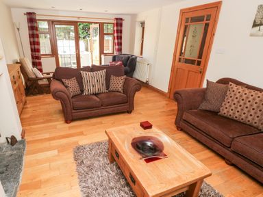 A living room with brown sofas a wooden coffee table and glass door to outside at Ty Melyn in Boncath