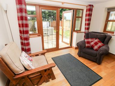 A living room with wooden furniture cushioned chairs red plaid curtains and glass door leading outside at Ty Melyn in Boncath