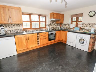 A kitchen with wooden cabinets dishwasher oven washing machine and clock on wall at Ty Melyn in Boncath