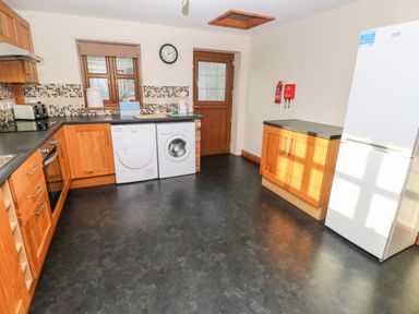 A kitchen with wooden cabinets washing machine dryer oven and white refrigerator at Ty Melyn in Boncath