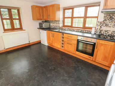 A kitchen with wooden cabinets a built-in oven a microwave a dishwasher and two windows at Ty Melyn in Boncath