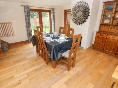 A dining room with a wooden table set with bowls plates and glasses surrounded by wooden chairs near glass doors at Ty Melyn in Boncath