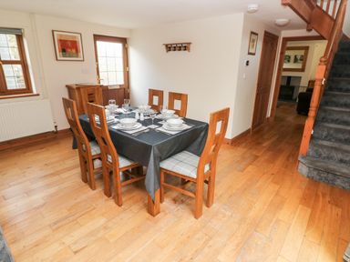 A dining room with a set table and wooden chairs near a staircase at Ty Melyn in Boncath