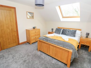 A bedroom with a wooden bed frame bed with pillows and blankets two wooden bedside tables with lamps a wooden chest of drawers a wooden door and a skylight window at Ty Melyn in Boncath