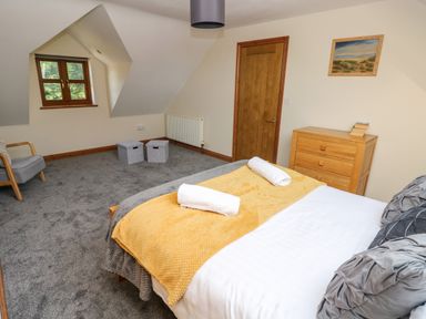 A bedroom with a bed with towels on a blanket a wooden dresser a chair and a window at Ty Melyn in Boncath