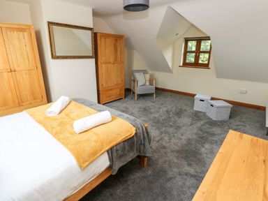 A bedroom with a bed with towels and blankets wooden wardrobes a chair and storage boxes at Ty Melyn in Boncath