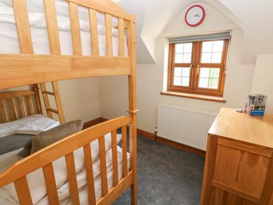 A bedroom with a wooden bunk bed a wooden dresser a window with a clock above it and a radiator below at Ty Melyn in Boncath