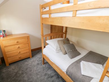 A bedroom with a wooden bunk bed and a wooden chest of drawers on a grey carpeted floor at Ty Melyn in Boncath