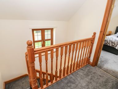 A stair landing with wooden banisters and a window with a view of a garden at Ty Melyn in Boncath