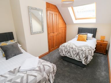 A bedroom with two single beds a nightstand a lamp a mirror and a skylight window at Ty Melyn in Boncath