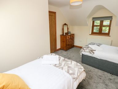 A bedroom with two single beds a wooden dresser with a mirror a window and a door at Ty Melyn in Boncath
