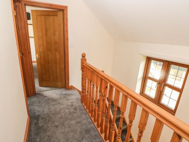 A hallway with wooden banister stair railing grey carpet and a wooden door at Ty Melyn in Boncath