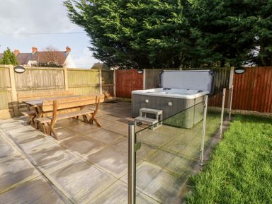 A backyard with a wooden picnic table bench set hot tub enclosed by glass fencing and grass area at Ty Melyn in Boncath