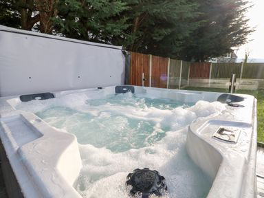 An outdoor hot tub with bubbling water next to a wooden fence and trees at Ty Melyn in Boncath