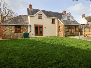 A two-story house with stone and brick exterior walls a tiled roof green grass lawn and wooden framed windows at Ty Melyn in Boncath