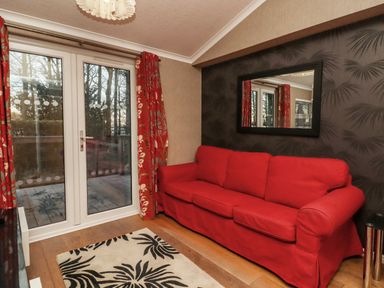 A room with a red sofa next to glass doors with red curtains and a black patterned wall with a mirror at Swinsty Lodge in Fewston near Darley
