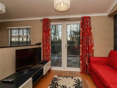 A living room with a red sofa a television on a black and white stand and glass doors with red curtains at Swinsty Lodge in Fewston near Darley