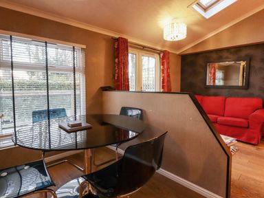 A dining area with a glass table and black chairs next to a window and a living room with a red sofa and wall mirror at Swinsty Lodge in Fewston near Darley