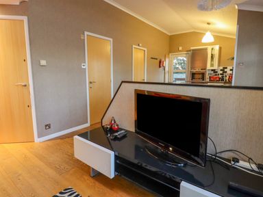 A living area with a television on a black and white stand wooden doors and a view into a kitchen at Swinsty Lodge in Fewston near Darley
