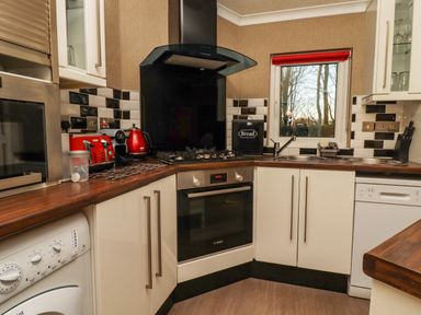 A kitchen with white cabinets a gas stove an oven a microwave a washing machine a dishwasher a sink and red appliances at Swinsty Lodge in Fewston near Darley