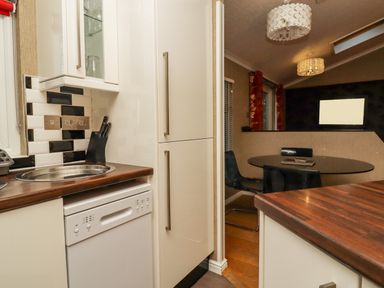 A compact kitchen with white cabinets a round stainless steel sink and a black and white backsplash next to a dining area with a black round table black chairs and pendant lights at Swinsty Lodge in Fewston near Darley