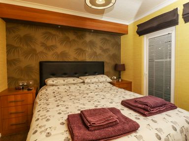 A bedroom with a double bed with patterned bedding and two stacks of folded towels on top at Swinsty Lodge in Fewston near Darley