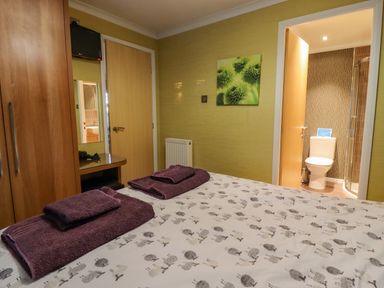 A bedroom with a bed covered in printed bedding and folded towels overlooking a door to a bathroom at Swinsty Lodge in Fewston near Darley