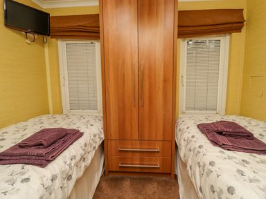 A bedroom with two single beds with folded towels on each bed a wooden wardrobe between the beds and a wall-mounted television at Swinsty Lodge in Fewston near Darley