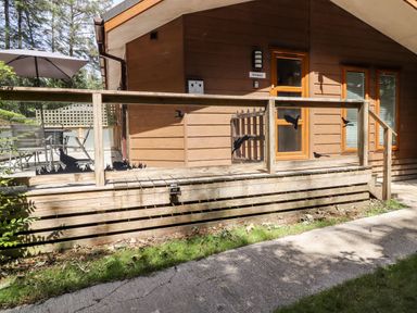 A wooden deck with outdoor furniture and umbrella beside a brown house with glass and wooden railings at Swinsty Lodge in Fewston near Darley