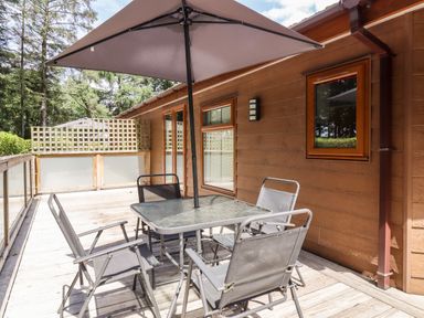 An outdoor patio with a glass table and four chairs under a large umbrella at Swinsty Lodge Fewston near Darley