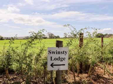 A signpost with swinsty lodge and arrow on a fence with green fields and trees in the background at Swinsty Lodge in Fewston near Darley