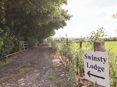 A gravel driveway between trees and a fence with a sign pointing to Swinsty Lodge in Fewston near Darley