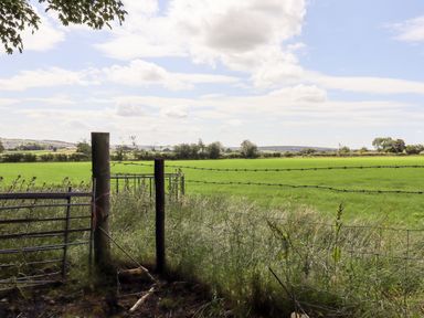 A green field behind a barbed wire fence with wooden posts under a partly cloudy sky at Swinsty Lodge in Fewston near Darley