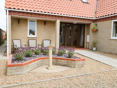 A patio area with a raised flower bed a stone pedestal and chairs at Drifters in Winterton-On-Sea