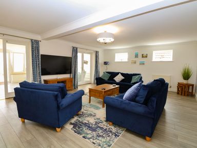 A living room with blue sofas a wooden coffee table and a wall mounted TV at Drifters in Winterton-On-Sea