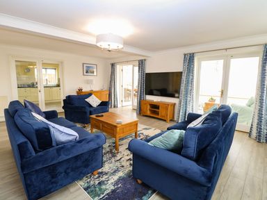 A living room with blue sofas a wooden coffee table and TV stand and large TV at Drifters in Winterton-On-Sea