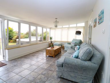 A sitting room with large windows a blue sofa armchair wooden coffee table and indoor plants at Drifters in Winterton-On-Sea