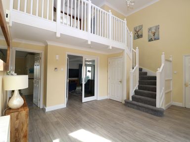An entryway with wooden flooring a carpeted staircase white railing two deer paintings a wooden table with a lamp and multiple white doors at Drifters in Winterton-On-Sea